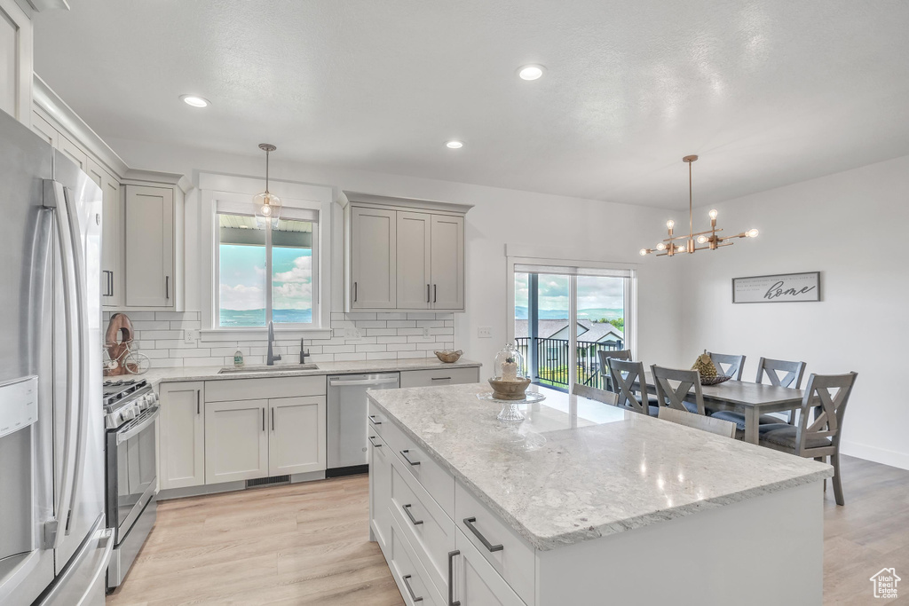 Kitchen with a kitchen island, tasteful backsplash, light wood-type flooring, appliances with stainless steel finishes, and sink