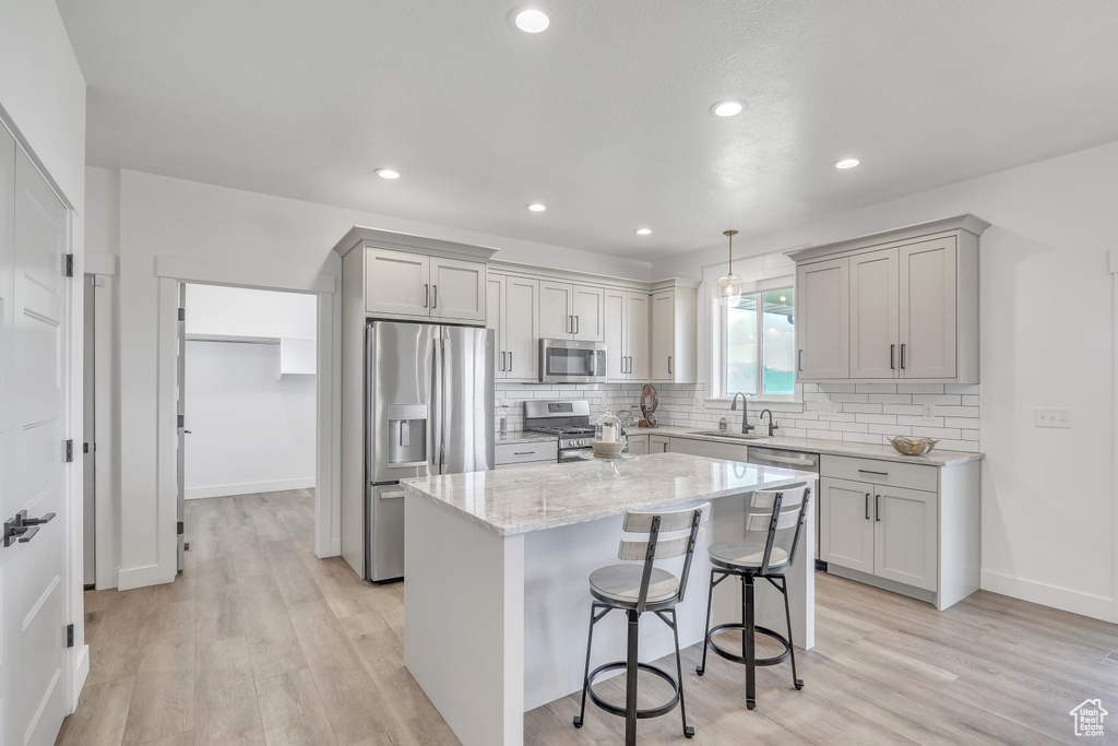 Kitchen with appliances with stainless steel finishes, light hardwood / wood-style floors, a kitchen island, and pendant lighting