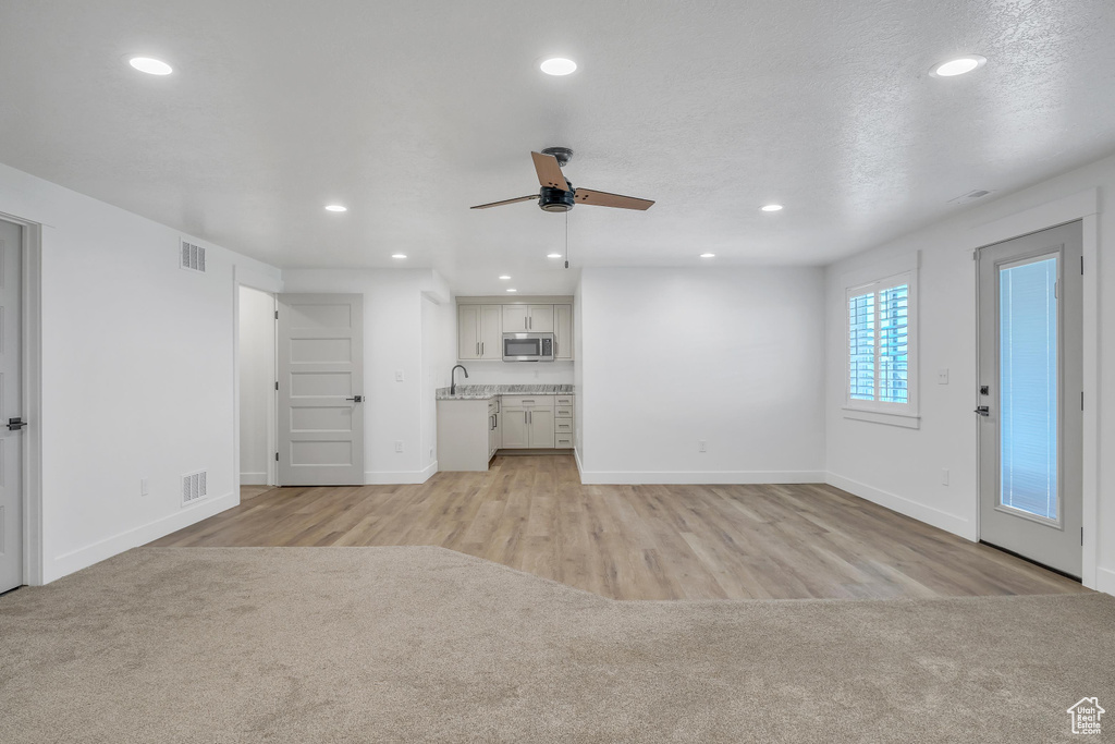 Unfurnished living room featuring ceiling fan, sink, and light hardwood / wood-style flooring