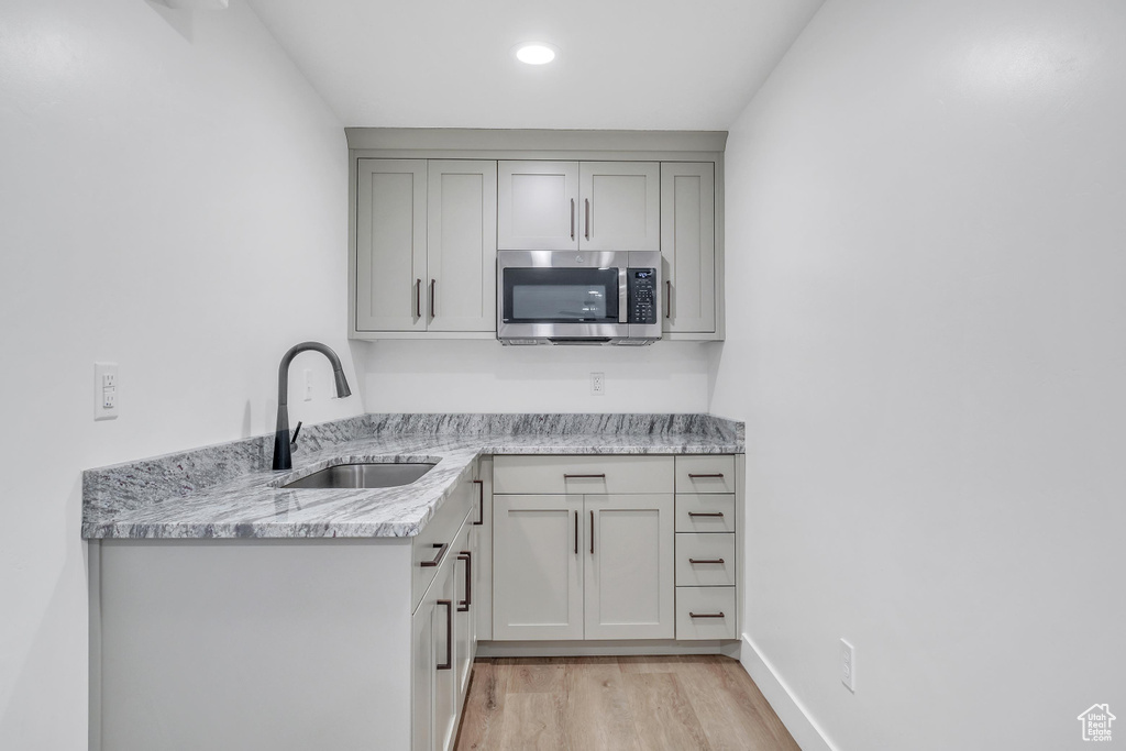 Kitchen with sink, light hardwood / wood-style floors, and light stone counters