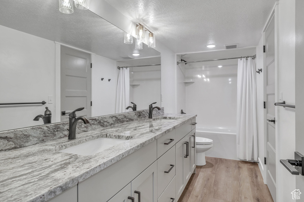 Full bathroom featuring shower / tub combo, wood-type flooring, a textured ceiling, toilet, and large vanity