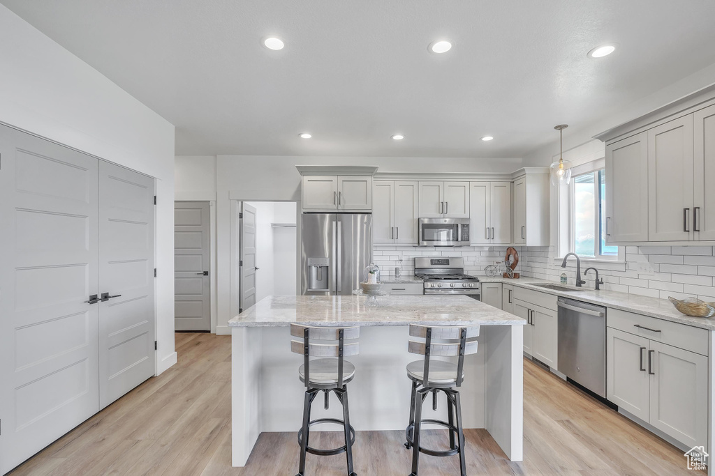 Kitchen with a kitchen island, hanging light fixtures, light wood-type flooring, and appliances with stainless steel finishes