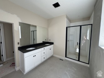 Full bathroom with double vanity, baseboards, a shower stall, and a sink