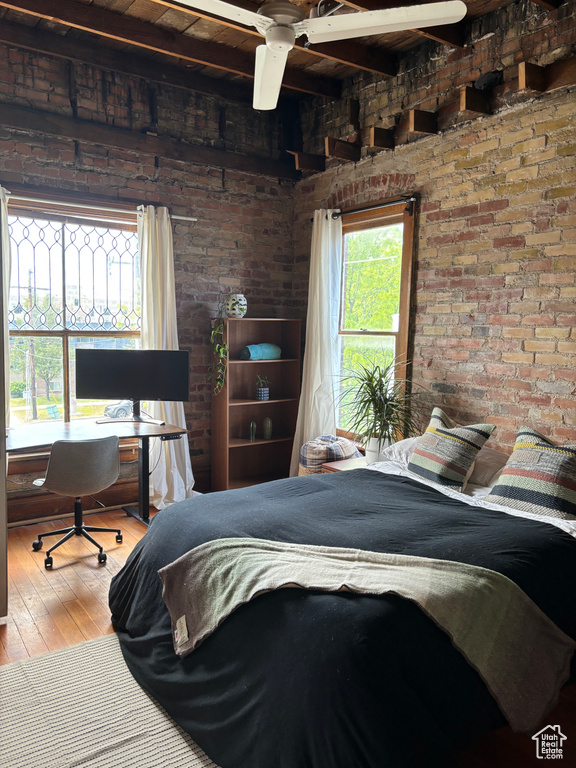 Bedroom featuring brick wall, beamed ceiling, and hardwood / wood-style flooring