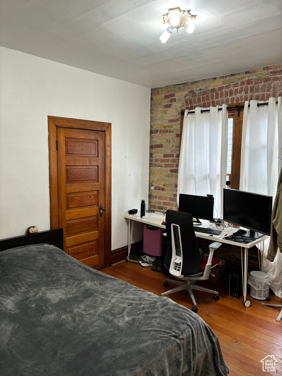 Bedroom featuring hardwood / wood-style flooring and brick wall