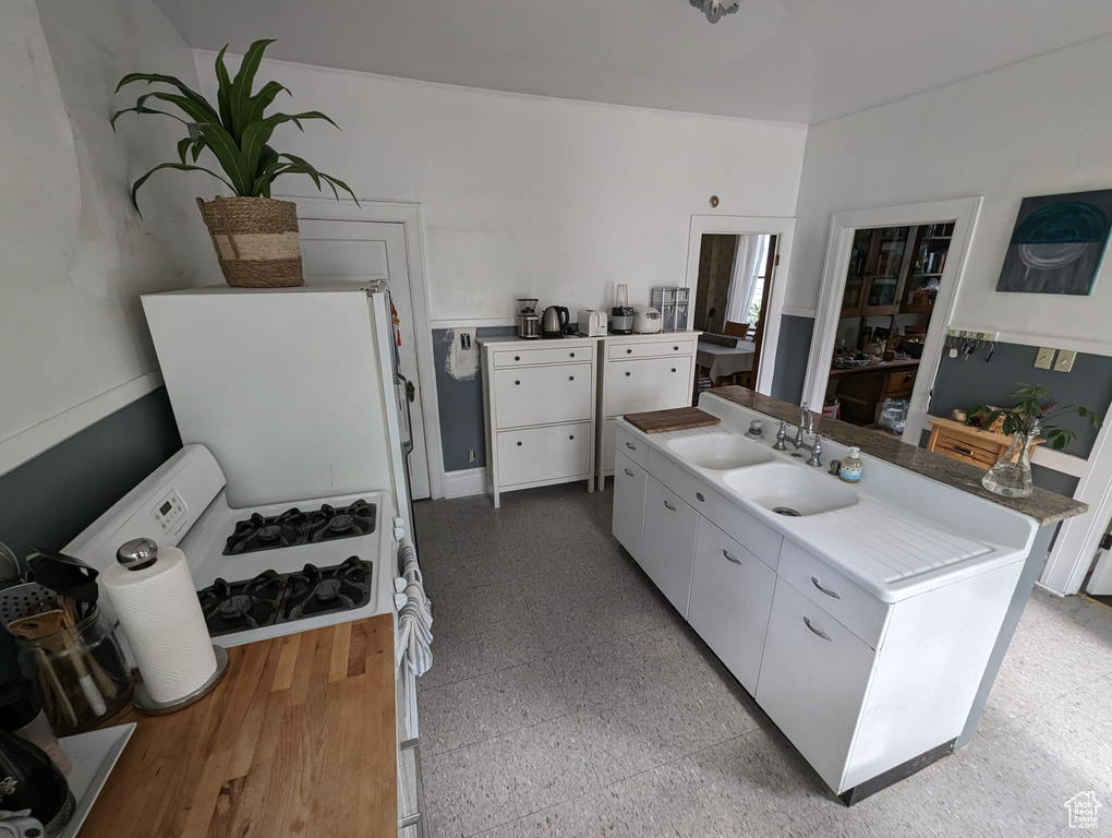 Kitchen with sink, white cabinets, white fridge, and light tile floors