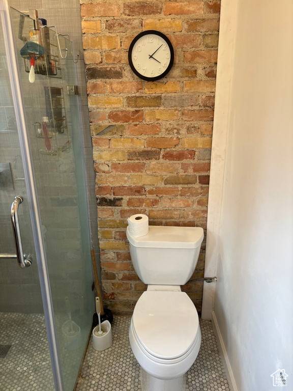 Bathroom featuring a shower with shower door, tile flooring, brick wall, and toilet