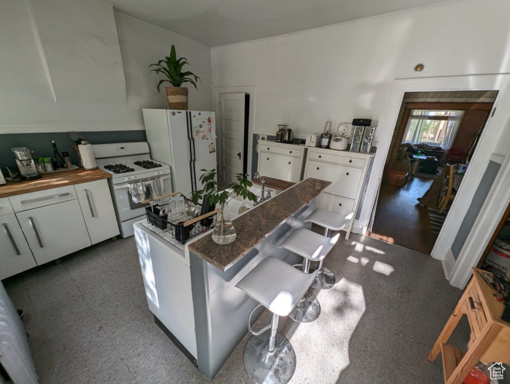 Kitchen featuring tile flooring, white appliances, dark stone countertops, a breakfast bar area, and white cabinetry