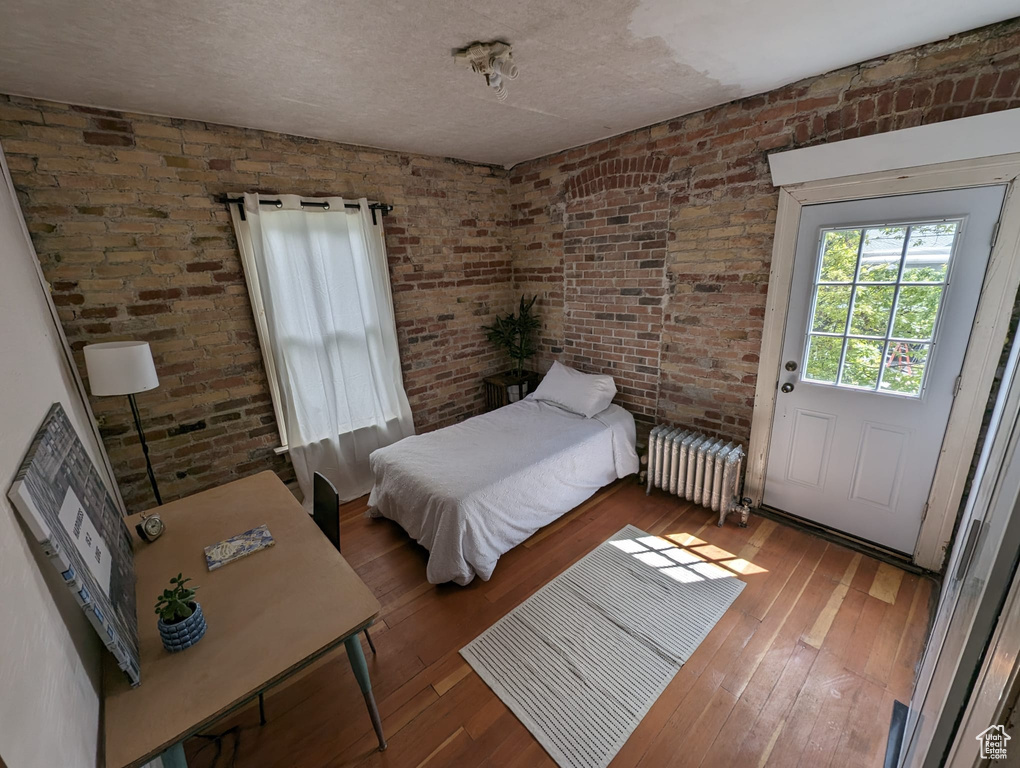 Bedroom with brick wall, a textured ceiling, hardwood / wood-style flooring, and radiator