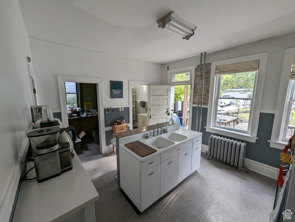 Kitchen featuring a center island with sink, tile floors, sink, white cabinets, and radiator