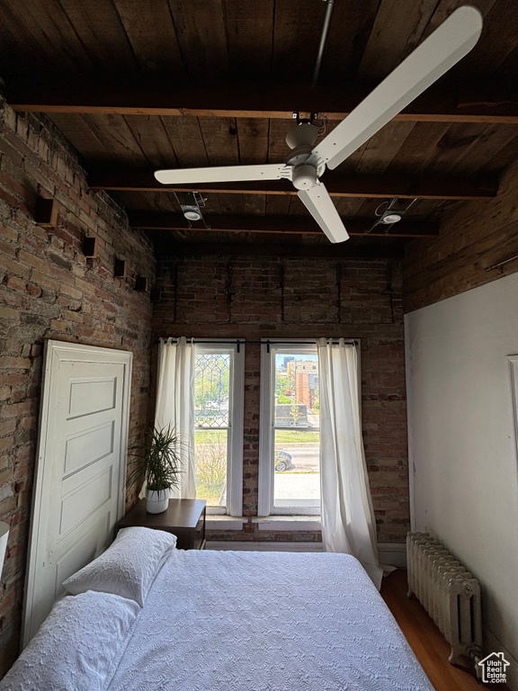 Bedroom with brick wall, beam ceiling, radiator heating unit, and wooden ceiling