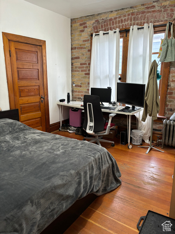 Bedroom with brick wall and hardwood / wood-style floors