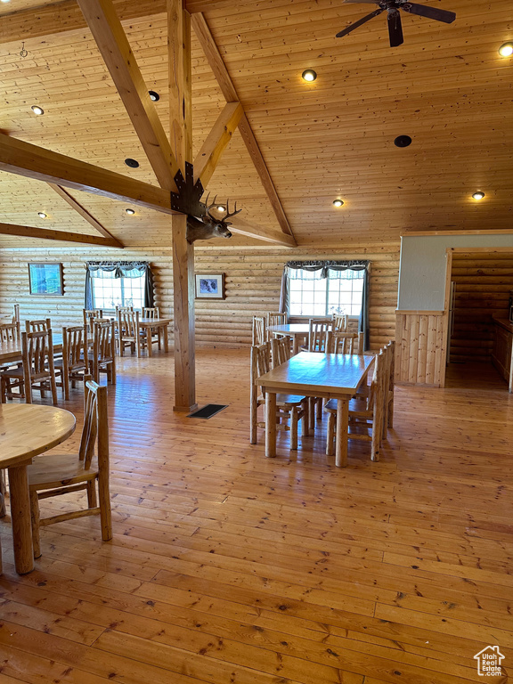 Dining space with vaulted ceiling with beams, wooden ceiling, hardwood / wood-style flooring, rustic walls, and ceiling fan