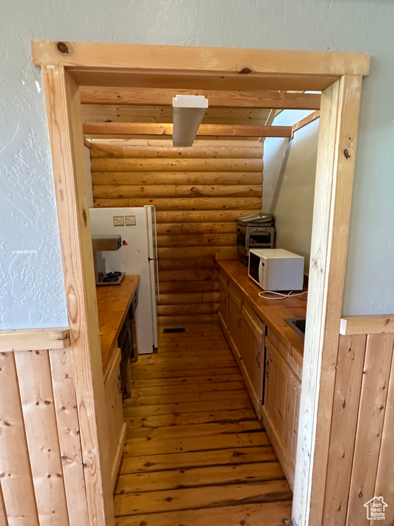 Kitchen with white appliances, log walls, and hardwood / wood-style flooring