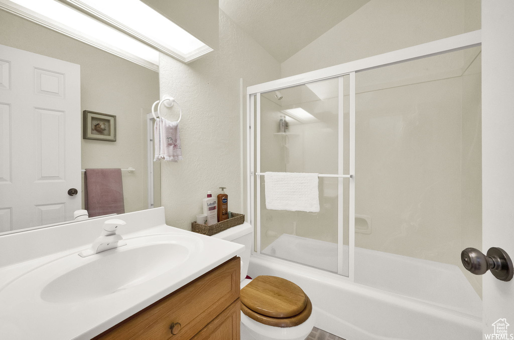 Full bathroom featuring shower / bath combination with glass door, lofted ceiling, toilet, and large vanity