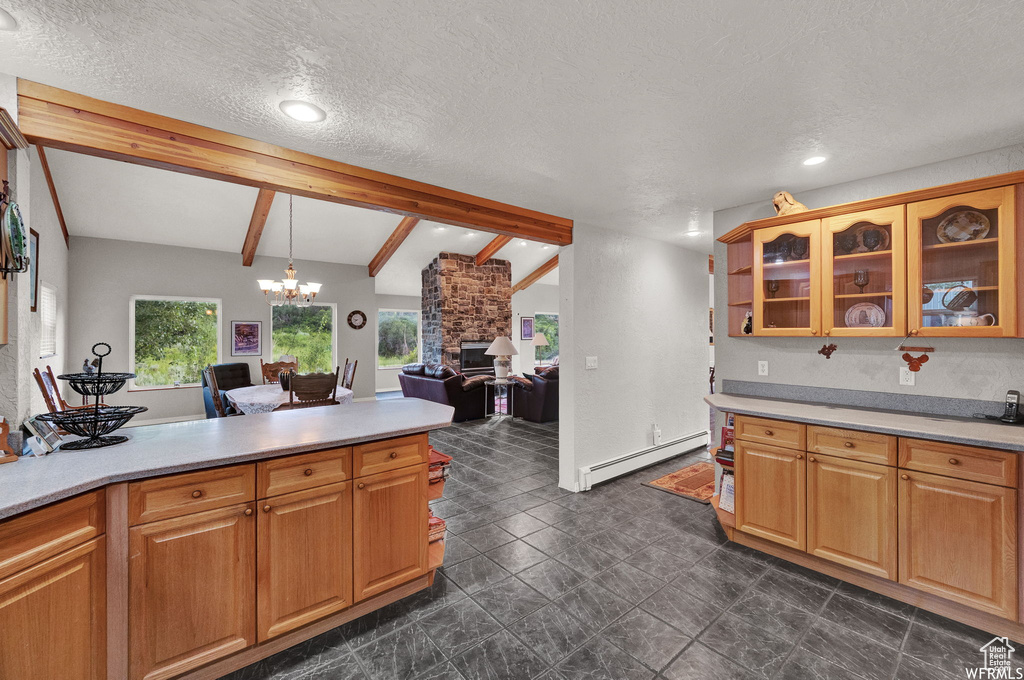 Kitchen with dark tile floors, a baseboard heating unit, a stone fireplace, lofted ceiling with beams, and a textured ceiling