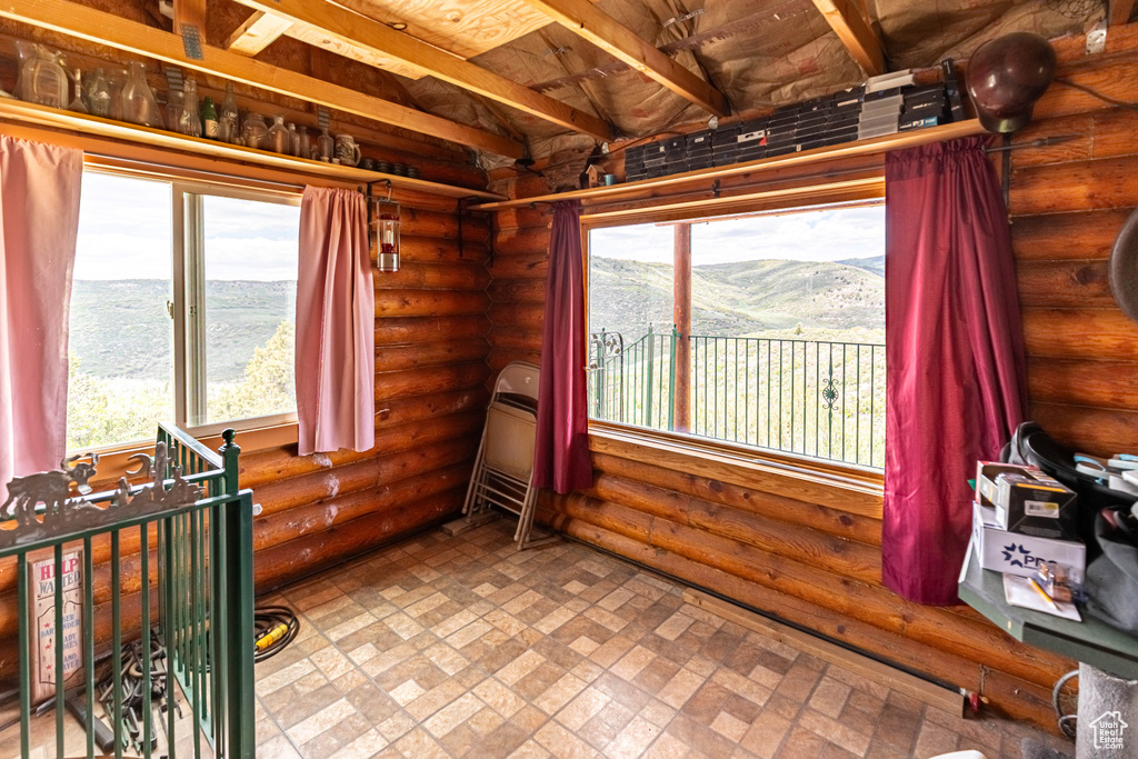 Interior space featuring tile flooring, rustic walls, a mountain view, and beam ceiling