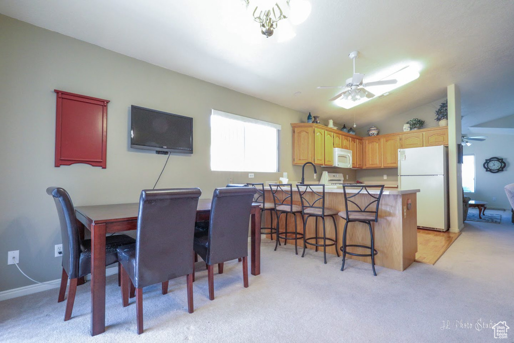 Dining space featuring vaulted ceiling, light carpet, sink, and ceiling fan