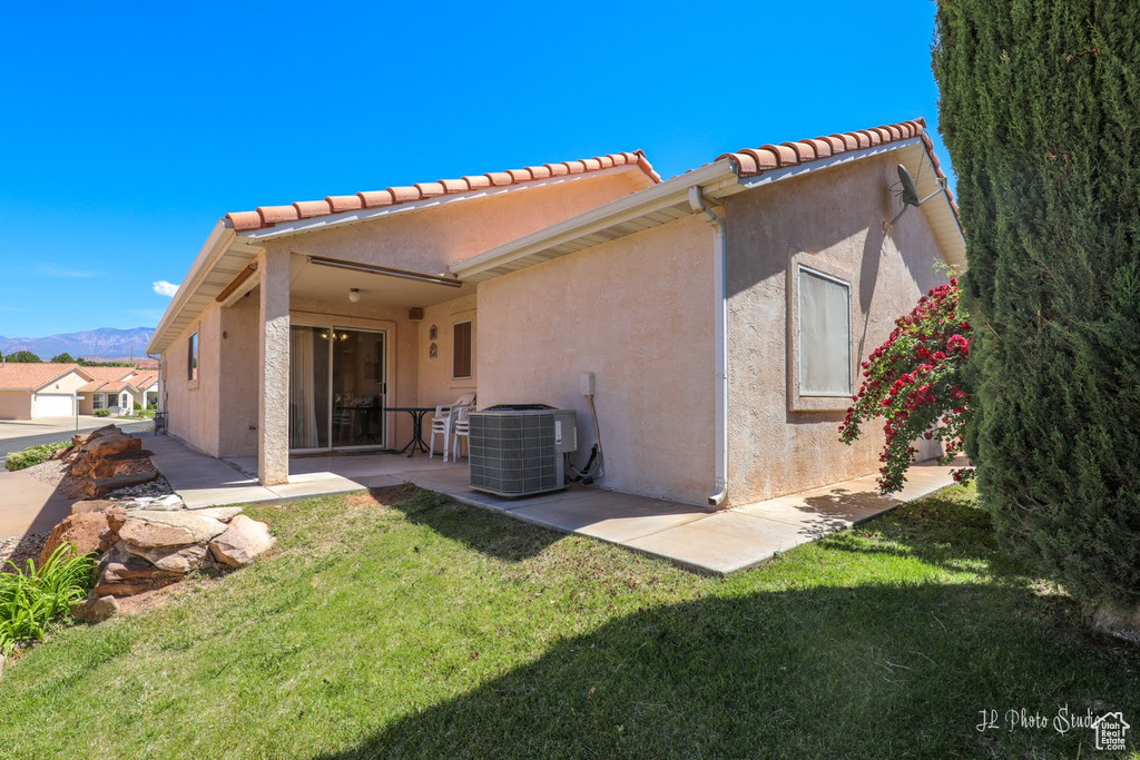 Rear view of property with a patio area, central air condition unit, and a lawn