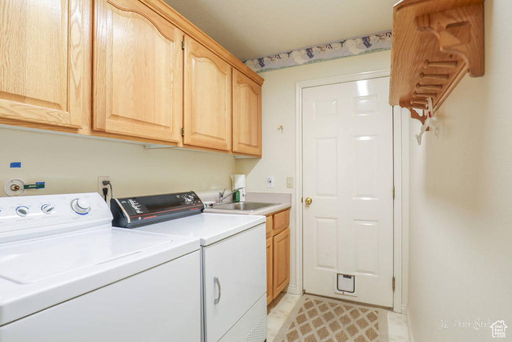 Clothes washing area with washing machine and dryer, sink, cabinets, and light tile floors