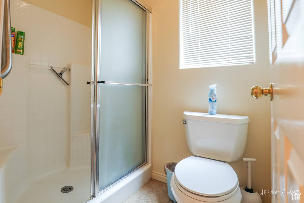 Bathroom featuring a shower with shower door, tile flooring, and toilet