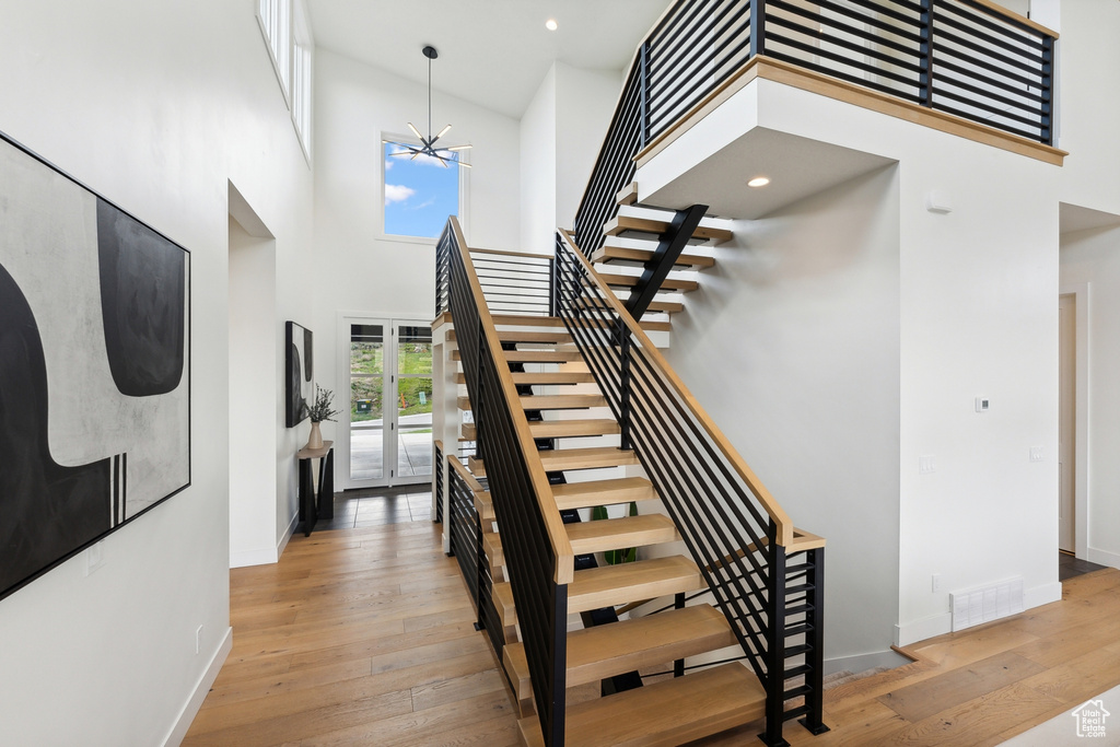 Staircase with a towering ceiling, light hardwood / wood-style flooring, and an inviting chandelier