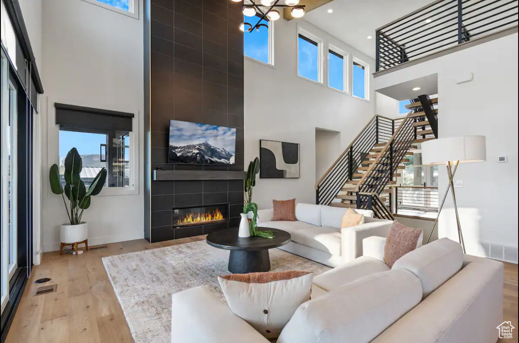 Living room featuring light hardwood / wood-style floors, a tiled fireplace, a notable chandelier, and a high ceiling