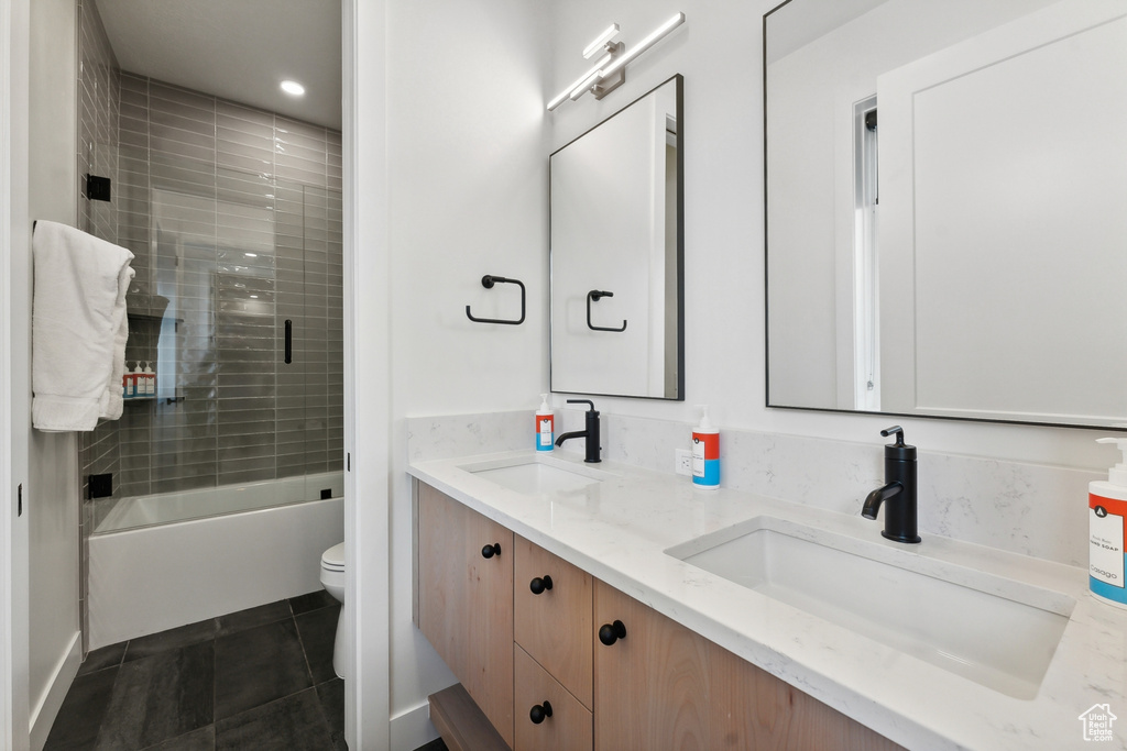 Full bathroom with dual sinks, shower / bath combination with glass door, tile floors, toilet, and large vanity