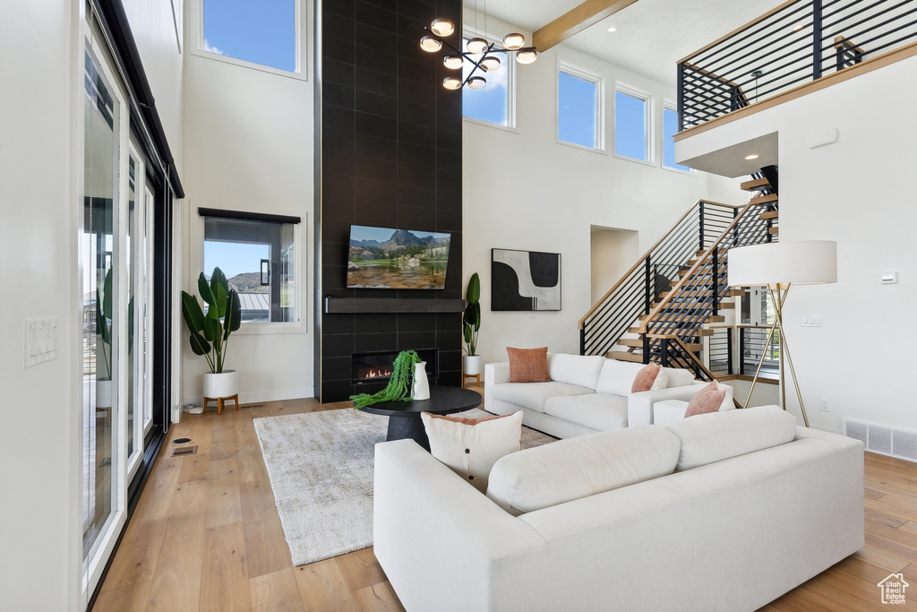 Living room featuring beam ceiling, a towering ceiling, light wood-type flooring, and a chandelier