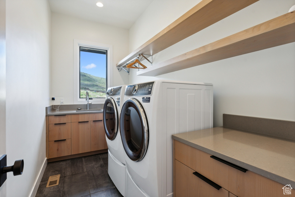 Washroom with sink, washer and clothes dryer, dark tile floors, and cabinets