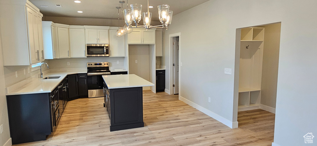 Kitchen featuring a center island, sink, white cabinetry, appliances with stainless steel finishes, and decorative light fixtures