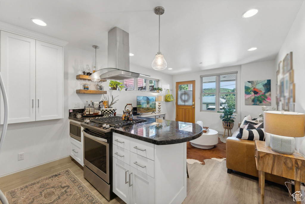 Kitchen with dark stone counters, light hardwood / wood-style flooring, stainless steel appliances, island exhaust hood, and white cabinets