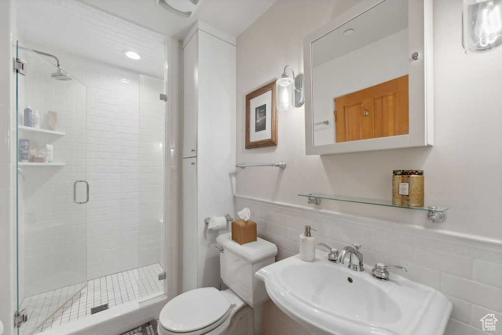 Bathroom with a shower with door, backsplash, tile walls, toilet, and sink