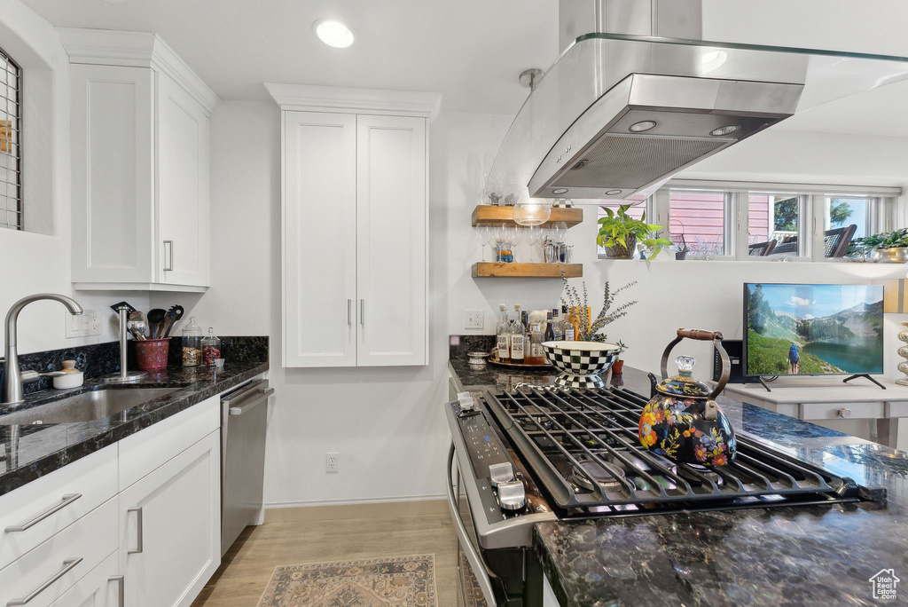 Kitchen featuring white cabinets, island range hood, dark stone counters, and sink