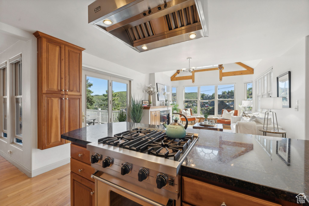 Kitchen featuring dark stone countertops, a chandelier, range hood, stainless steel stove, and light hardwood / wood-style floors