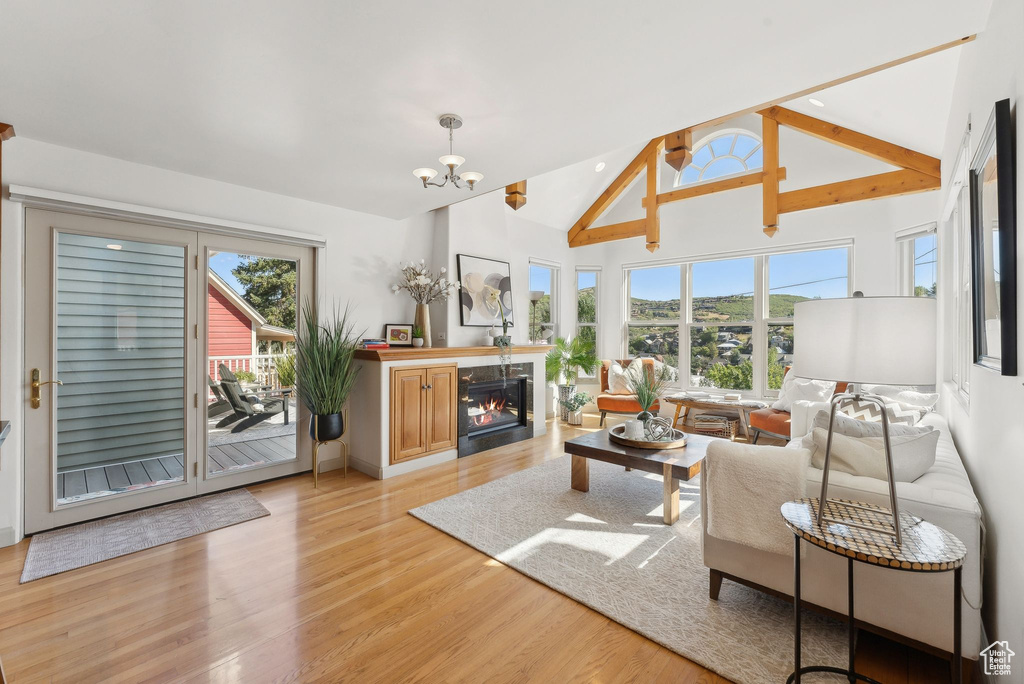 Living room with light wood-type flooring, a wealth of natural light, a chandelier, and vaulted ceiling with beams