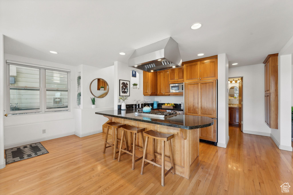 Kitchen featuring built in appliances, island range hood, kitchen peninsula, a breakfast bar area, and light hardwood / wood-style floors