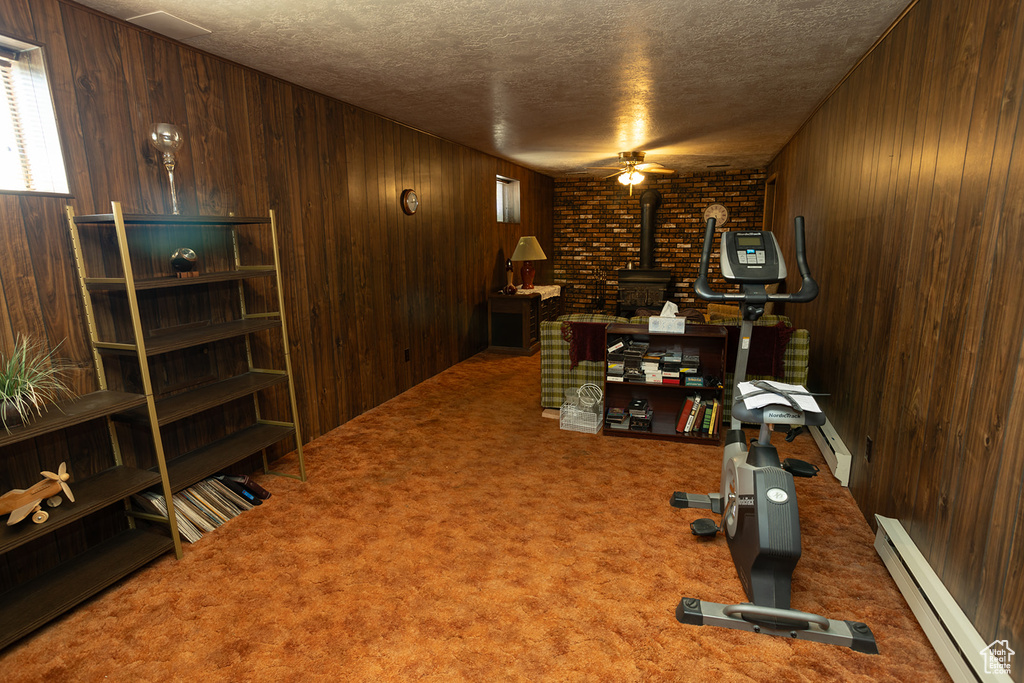 Workout room featuring brick wall, carpet, a wood stove, and a baseboard heating unit