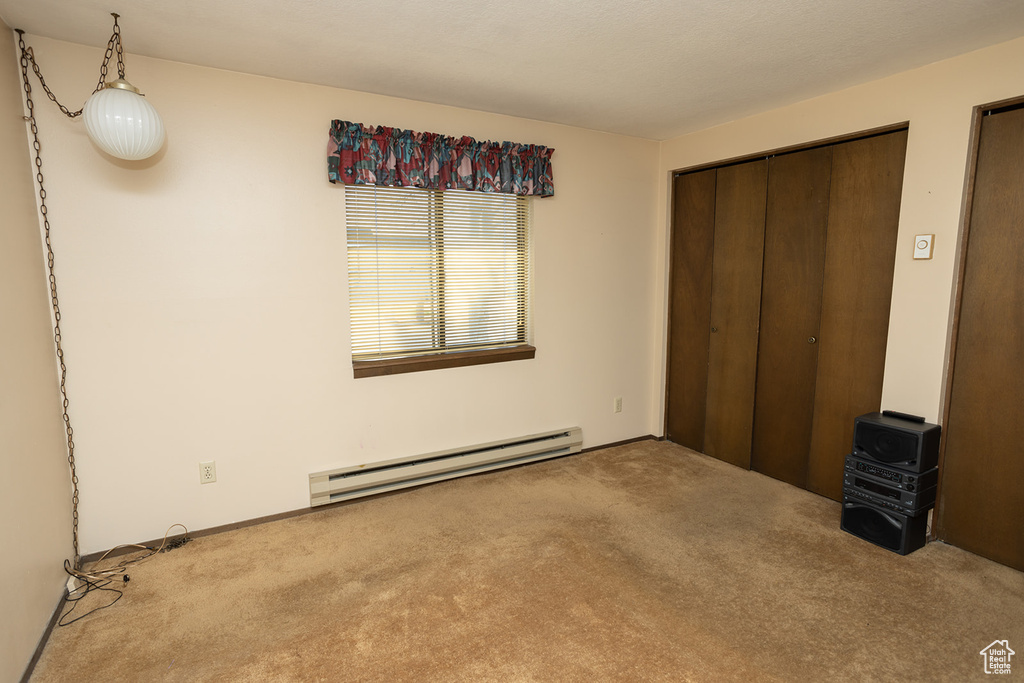 Unfurnished bedroom featuring baseboard heating and carpet flooring