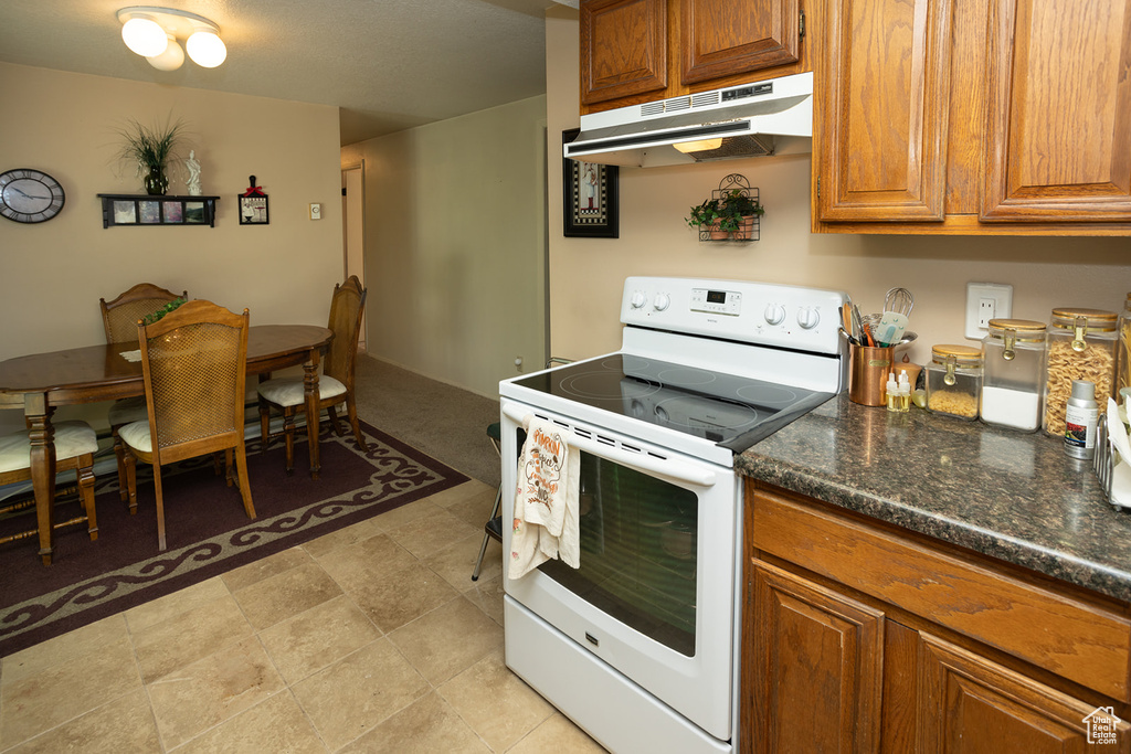 Kitchen featuring light tile flooring, white electric range oven, and dark stone countertops