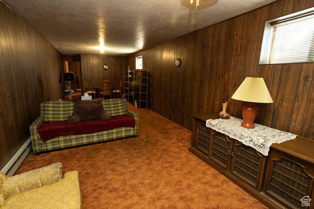 Living room featuring a baseboard heating unit, a textured ceiling, carpet flooring, and wooden walls