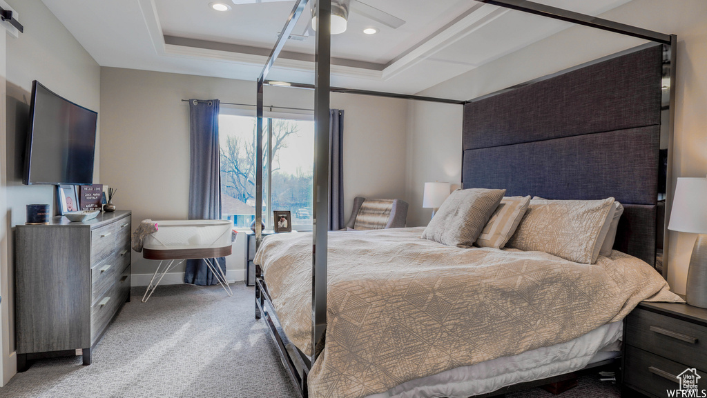 Carpeted bedroom featuring ceiling fan and a raised ceiling