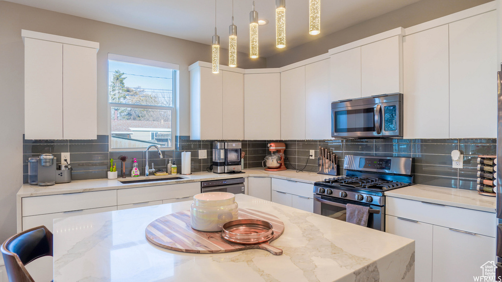 Kitchen with decorative light fixtures, white cabinets, tasteful backsplash, and appliances with stainless steel finishes