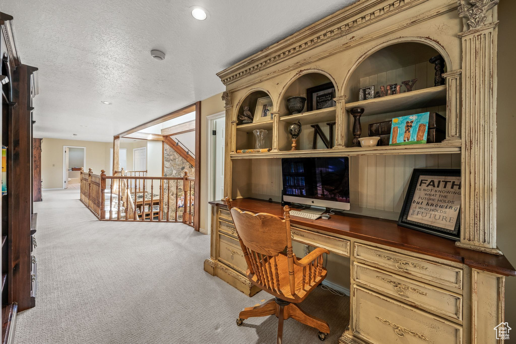 Carpeted office space with built in features, built in desk, and a textured ceiling