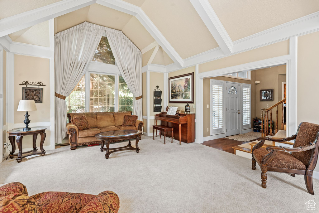 Carpeted living room with beamed ceiling, crown molding, and high vaulted ceiling