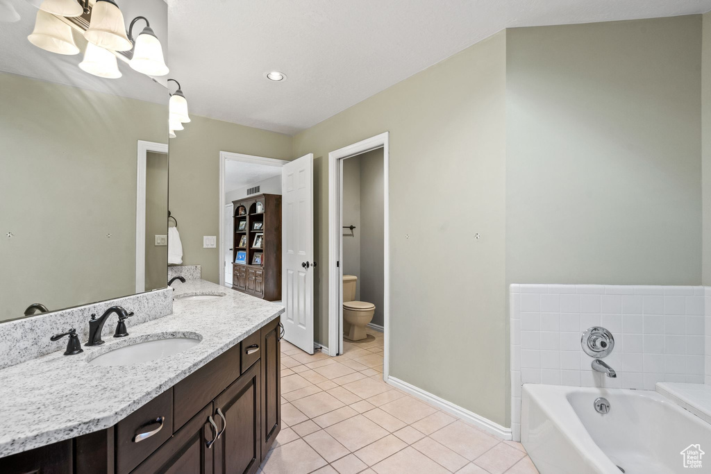 Bathroom featuring tile flooring, an inviting chandelier, a bathtub, vanity, and toilet