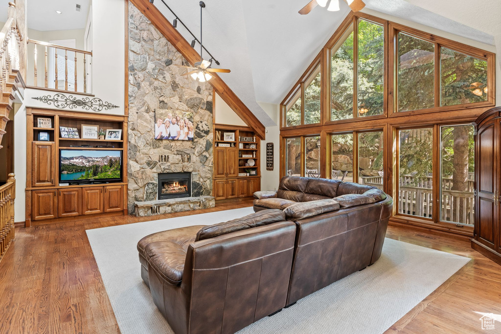 Living room featuring a stone fireplace, high vaulted ceiling, hardwood / wood-style flooring, and ceiling fan