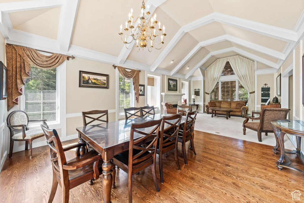 Dining area with a chandelier, a wealth of natural light, wood-type flooring, and vaulted ceiling with beams