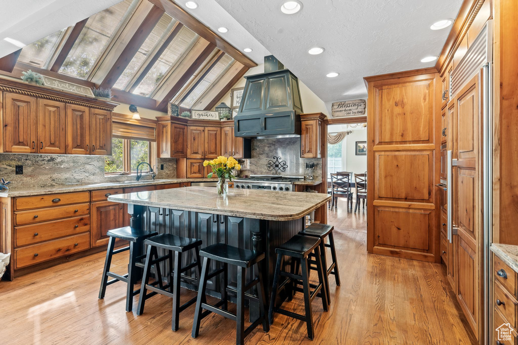 Kitchen featuring light stone countertops, a kitchen island, light wood-type flooring, custom range hood, and lofted ceiling with skylight