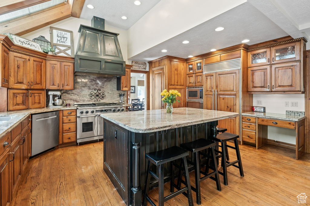 Kitchen featuring a center island, built in appliances, light wood-type flooring, and light stone counters